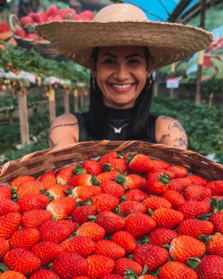 Mulher com chapéu de palha segurando cesta com muitos morangos