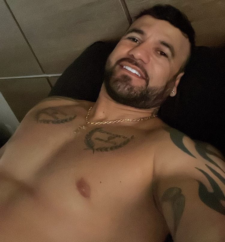 Selfie de Hadbala sem camisa usando corrente Dourada de Cruz deitado na cama
