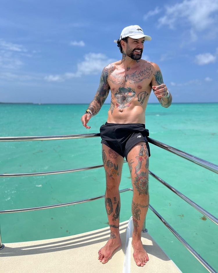 Wagner Santiago ex BBB na Privacy, só de bermuda Preta em embarcação em alto mar. ele é todo tatuado e também usa um boné branco