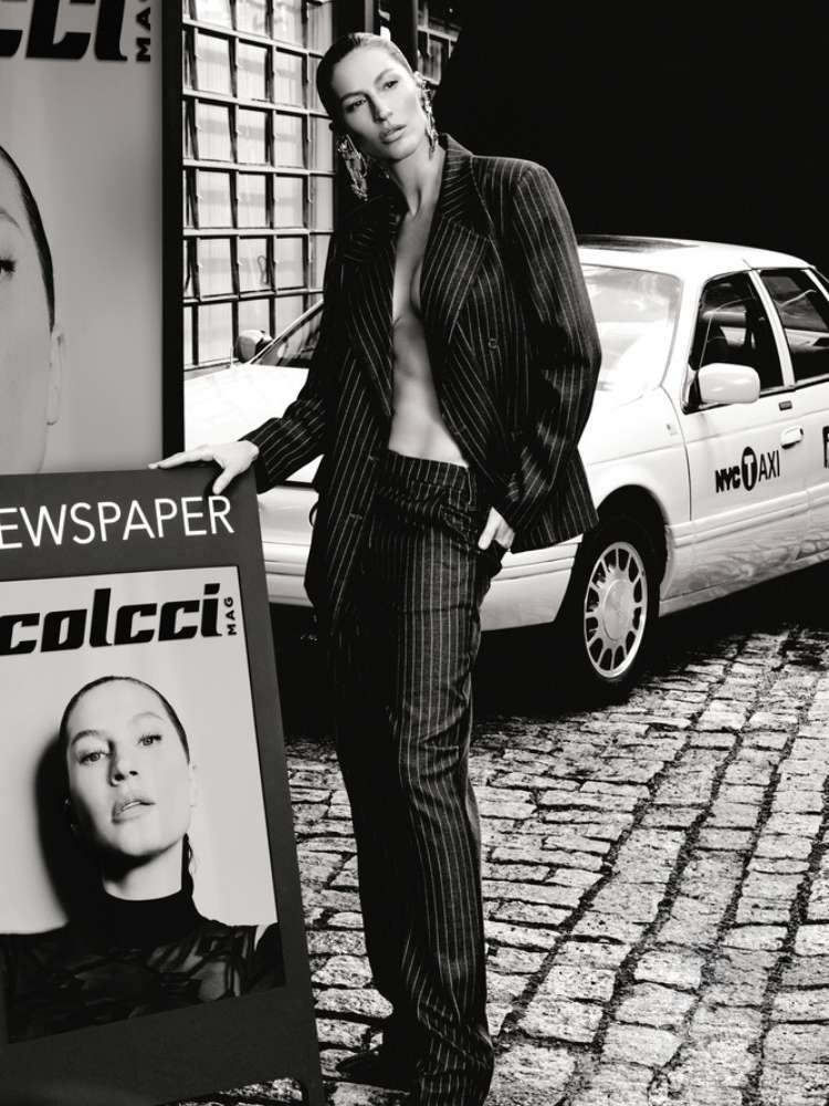 Foto em preto e branco de Gisele Bündchen usando blazer e calça em frente a um taxi e ao lado de um cartaz com seu rosto e o escrito "colcci"