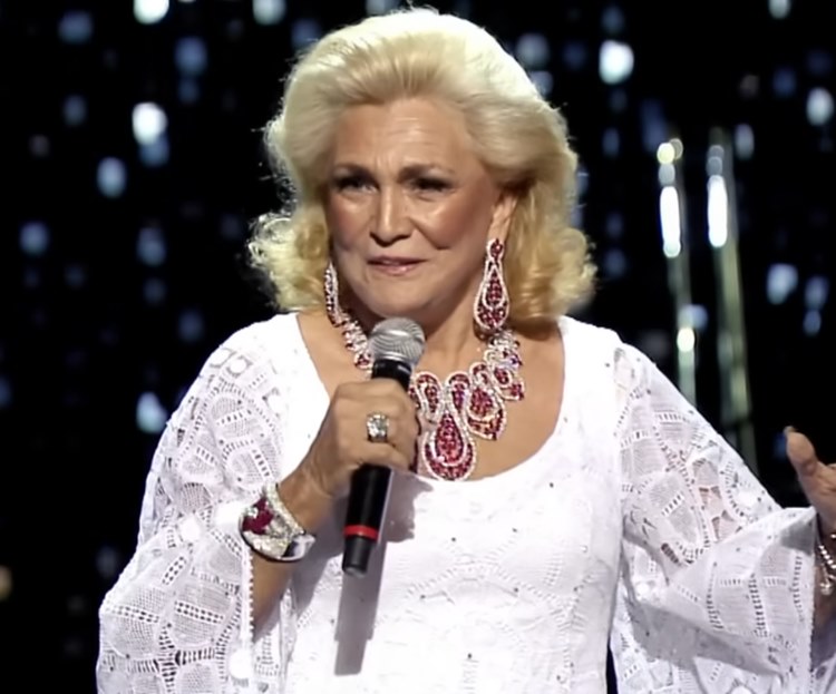 Hebe Camargo usando roupa branca e joias vermelhas cantando com Roberto Carlos que não aparece na foto