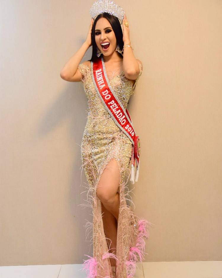 A participante do BBB 24 quando venceu o peladão 2018 usando coroa e faixa de rainha, Ela veste um vestido dourado com fenda e Plumas