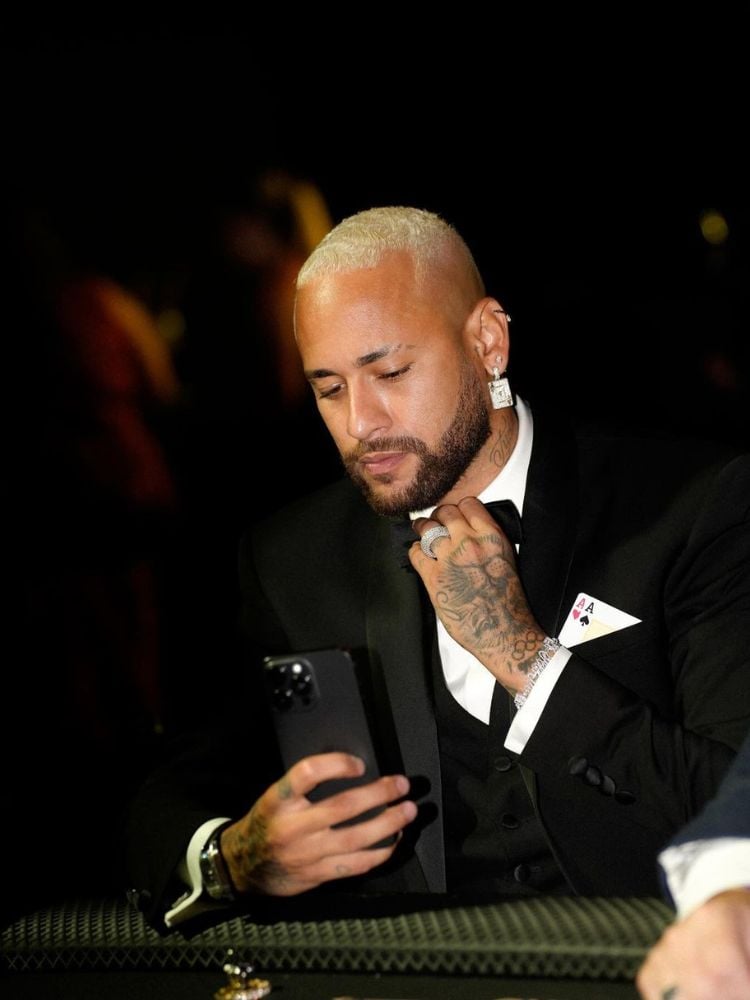 Neymar de terno preto segurando um Iphone