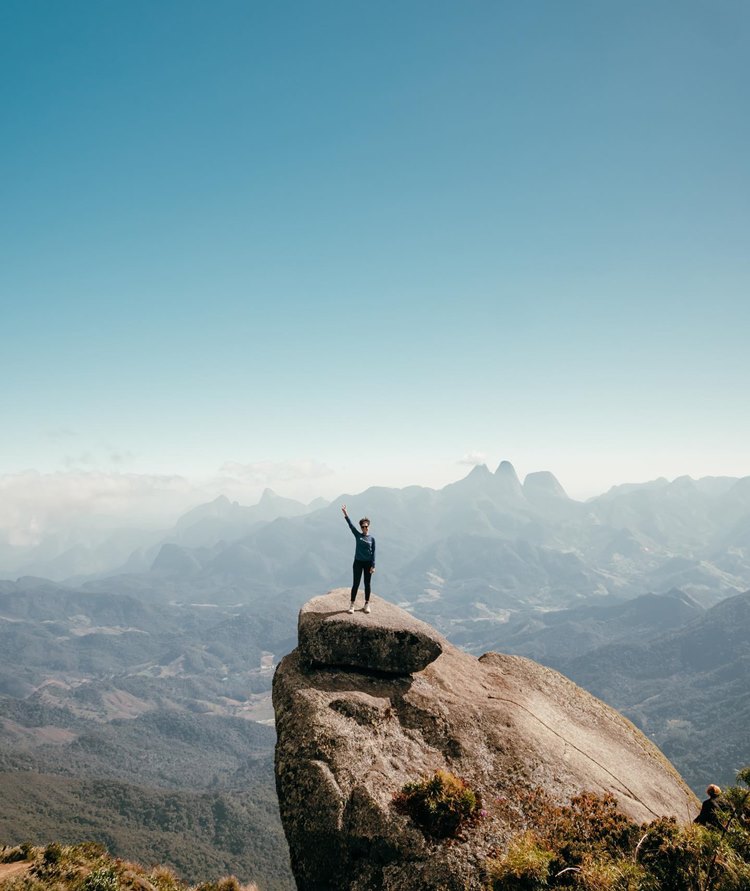 Mulher fazendo sinal de paz e amor no Pico da Caledônia, pedra localizada no Pico das Três Pedras, em Nova Friburgo