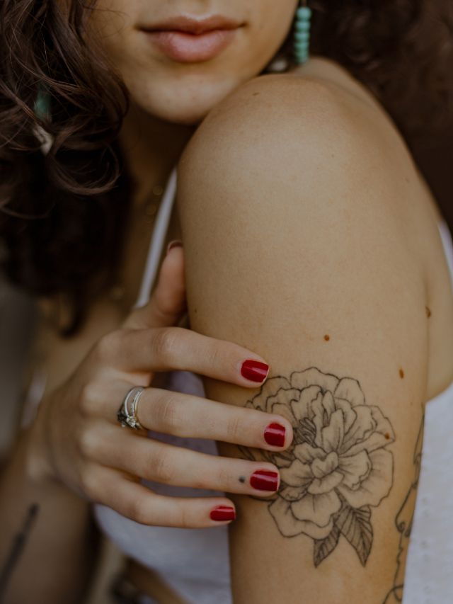 foto de mulher com unhas vermelhas tocando em tatuagem feminina de flor no braço