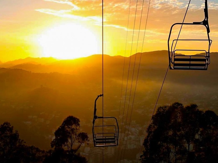 Foto do teleférico da Praça do Suspiro, com vista para montanhas durante o por do sol