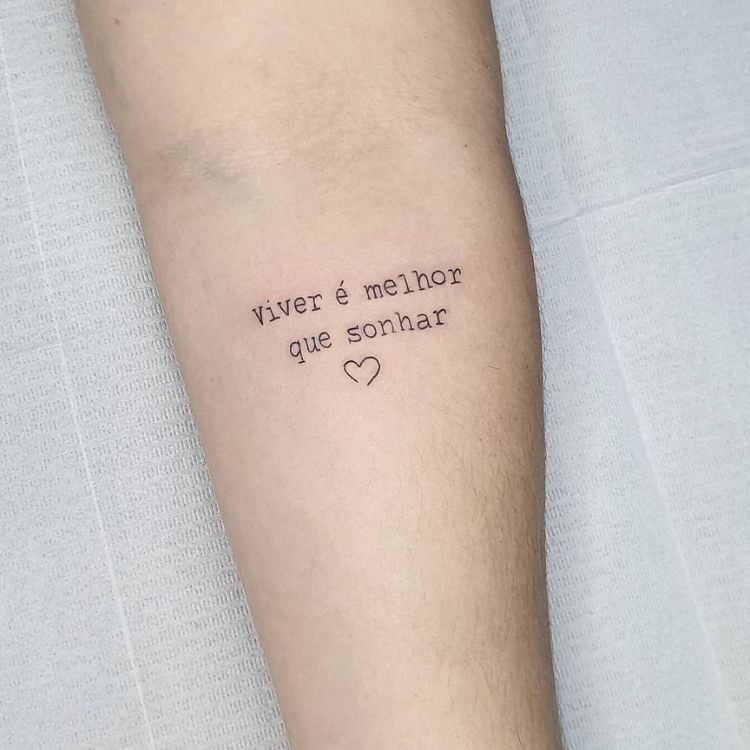 tatuagem no braço com a frase Viver é melhor que sonhar e um pequeno coração
