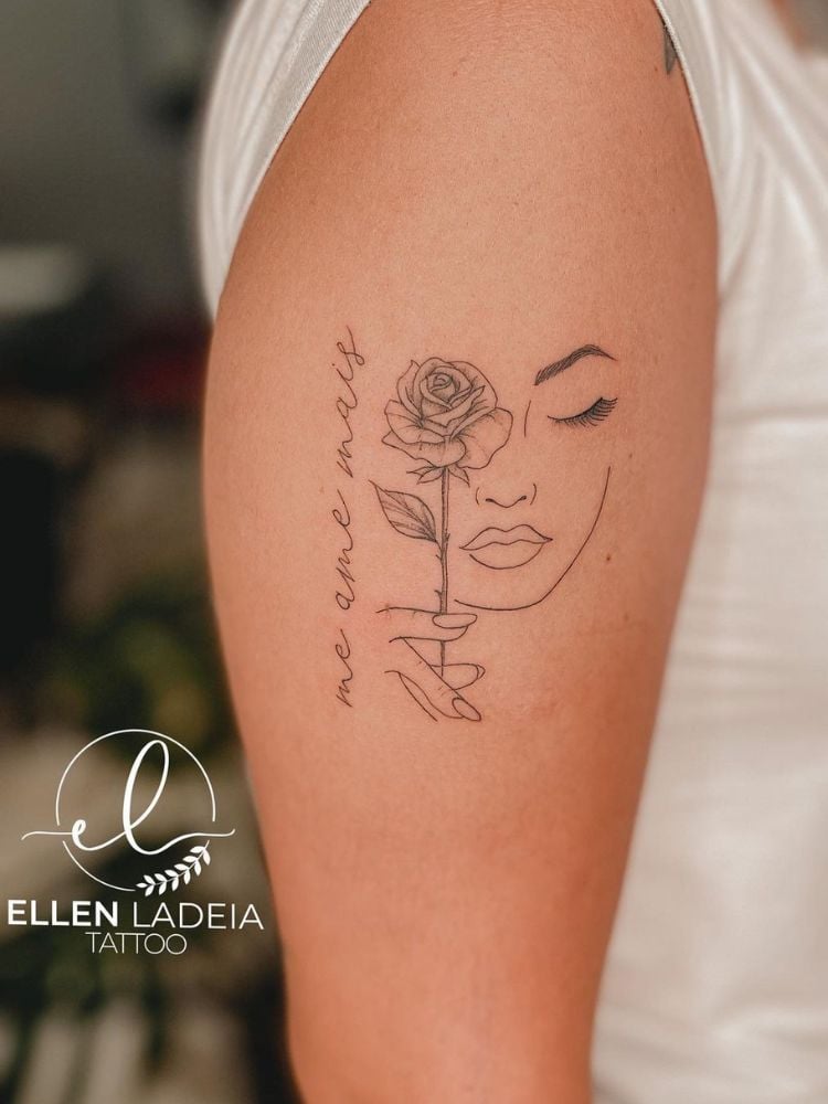 foto de braço de mulher com tatuagem de rosto feminino, rosa e frase Me ame mais