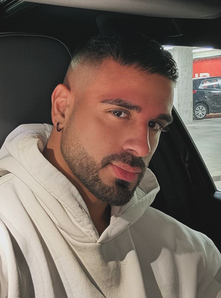 Homem com barba degradê, uma das tendências de 2024. Ele usa roupa branca e está dentro de carro