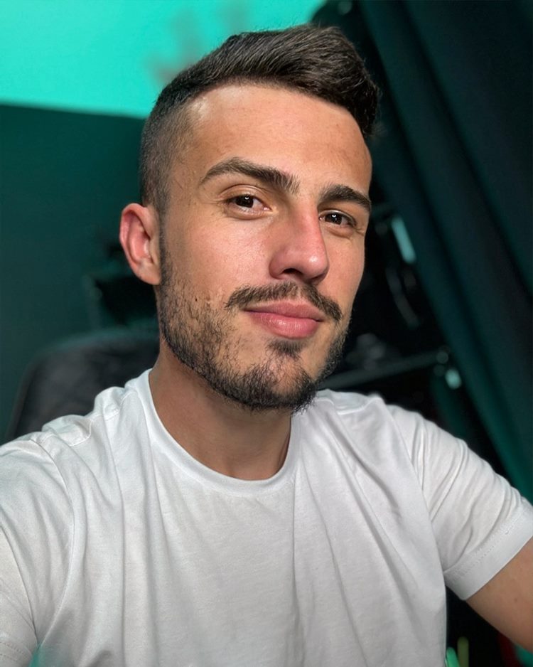 Homem com barba por fazer marcada, uma das tendências de 2024. Ele usa roupa branca e está sentado em uma cadeira