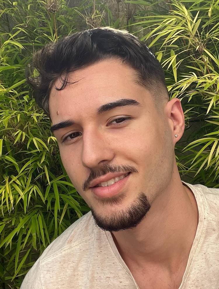 Homem com pelo do rosto estilo Van Dike, uma das tendências de 2024. Ele está com camiseta clara em fundo de planta verde