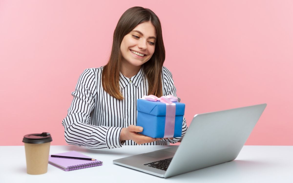 mulher segurando presente azul e rosa em frente a um notebook, simbolizando bônus jogo online