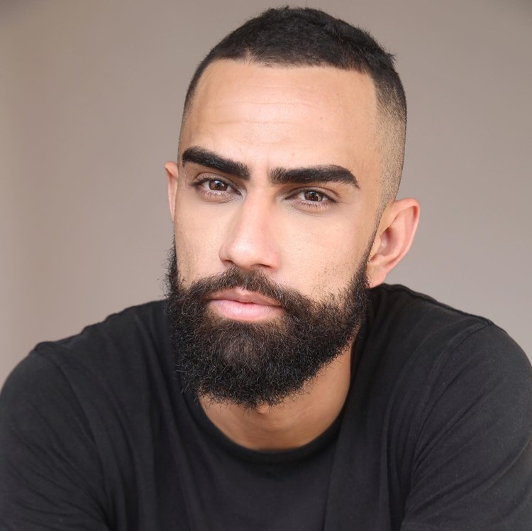 Homem com barba mais cheia no queixo, uma das tendências de 2024. Ele está com camisa preta em fundo cinza
