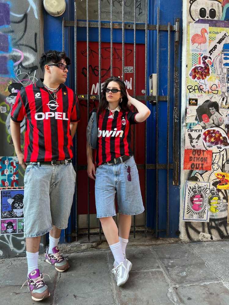 Homem e mulher de pele clara ambos usando camisa do Milan com bermuda jeans