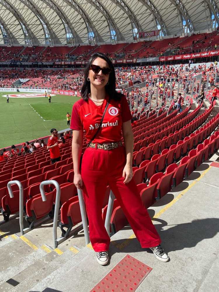 Mulher de pele clara no Beira-Rio usando camisa vermelha do Internacional, calça vermelha e cinto de onça