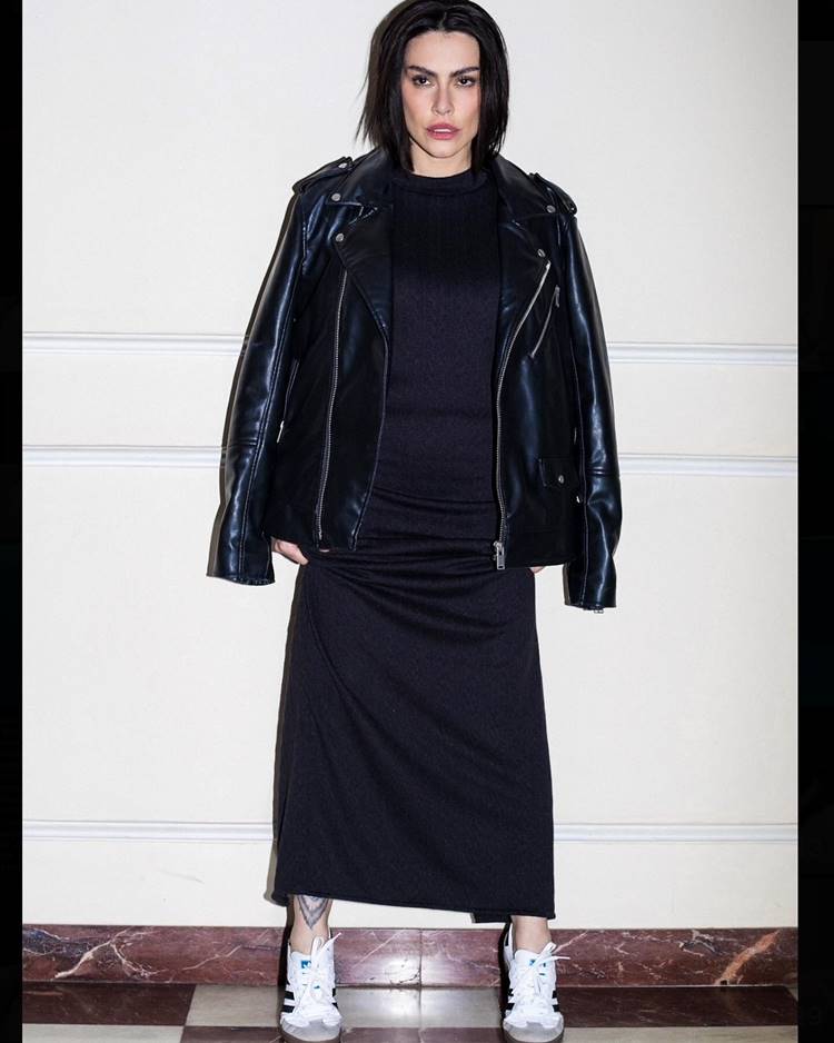 Estilo de Cleo Pires: Vestindo um vestido longo preto, jaqueta de couro preta e tênis, ela se destaca com um visual que mistura o formal com o casual, uma escolha audaciosa

