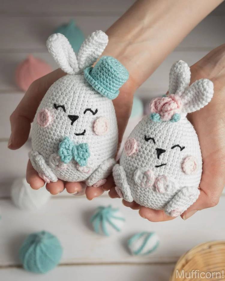 Mão segurando dois coelhinhos artesanais, confeccionados em formato de ovo de amigurumi, destacando-se pela técnica e criatividade.