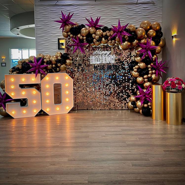 Painel dourado, grande placa de "50 anos", balões dourados e pretos, e estrelas pink.