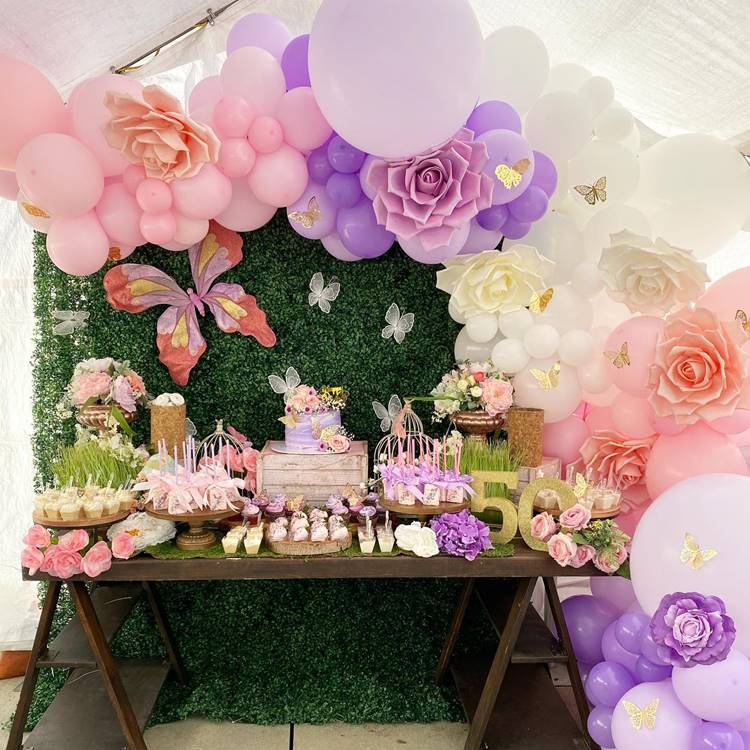 Festa com tema de borboleta para quem está fazendo 50 anos cores predominantes verde rosa roxo e branco mesa de madeira decorada com doces e bolo