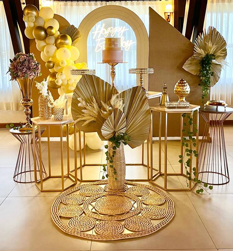 Nesta celebração de 50 anos, tudo resplandece em dourado, desde a decoração até o bolo central, ainda que os doces não estejam presentes. Uma placa ao fundo com a inscrição "Happy Birthday" completa o cenário luxuoso, celebrando o aniversário de forma majestosa e brilhante.