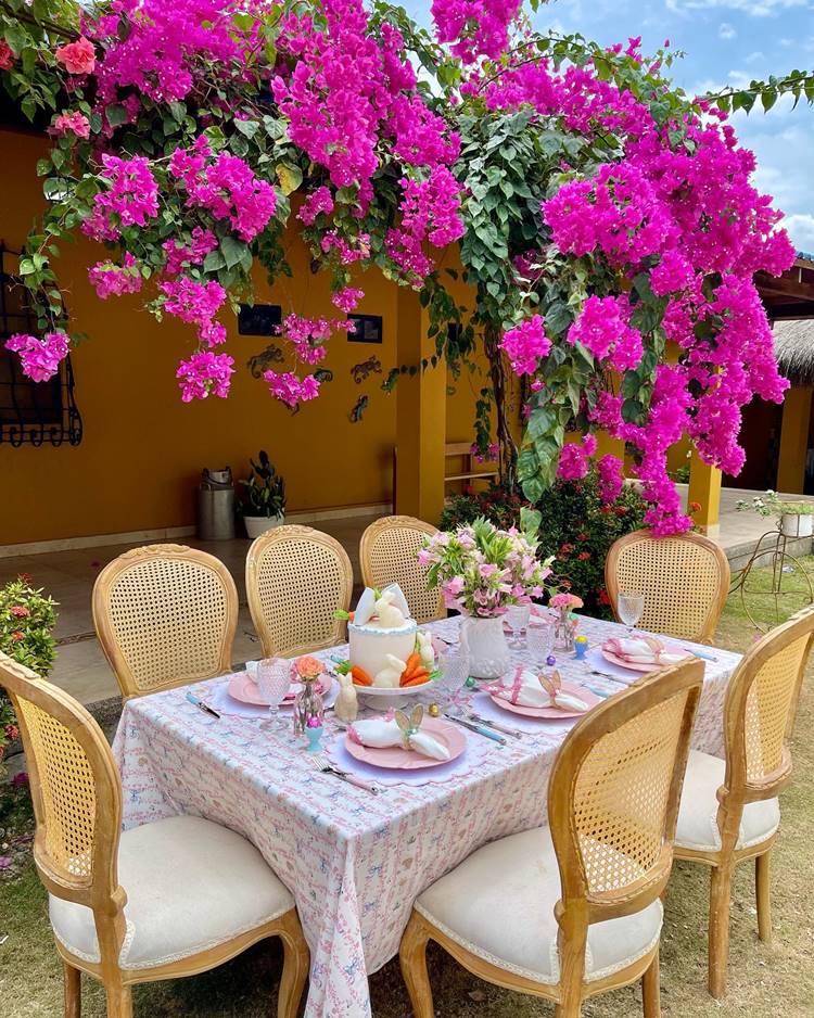  mesa posta de Páscoa para o almoço ao ar livre em casa com planta com flores roxas a mesa posta contém itens cor-de-rosa e branco