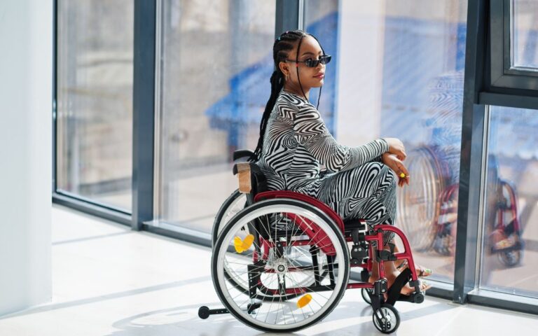 mulher negra em cadeira de rodas usando tranças no cabelo, óculos de sol e conjunto de zebra