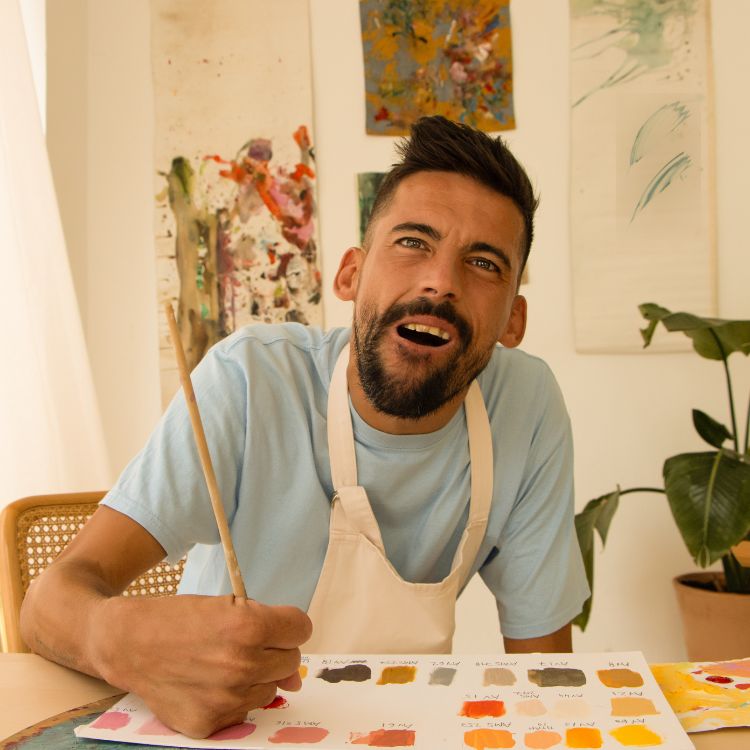 Homem PcD pintando com pincel e tinta em folha sob uma mesa