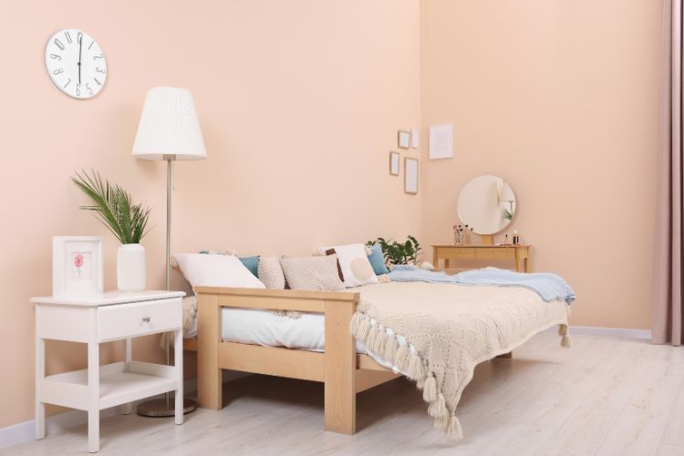 Quarto rosa claro com cama cheia de almofadas, móvel branco e abajur