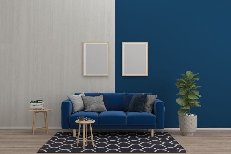 Sala com parede metade azul e metade madeira clara, com sofá azul, almofadas branca e cinza, planta e tapete de forma geométrica