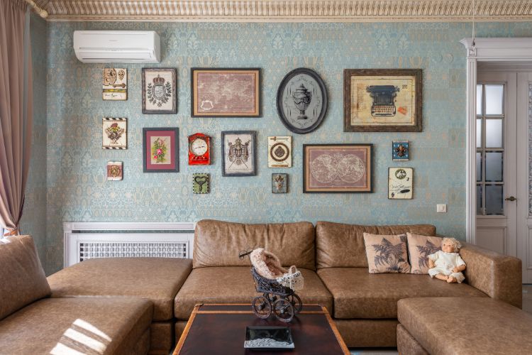 Sala com papel de parede azul, quadros retrôs, sofá de couro marrom e mesa de centro