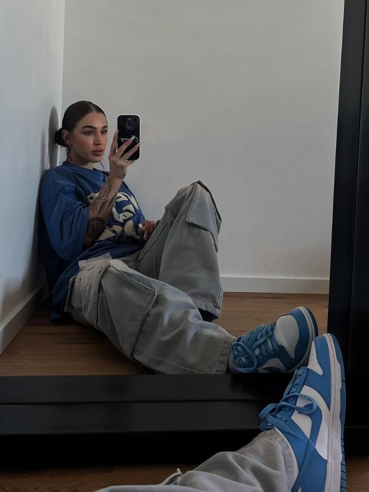 Mulher de pele clara tirando foto no espelho e usando blusa oversized azul, calça cargo e tênis nike azul