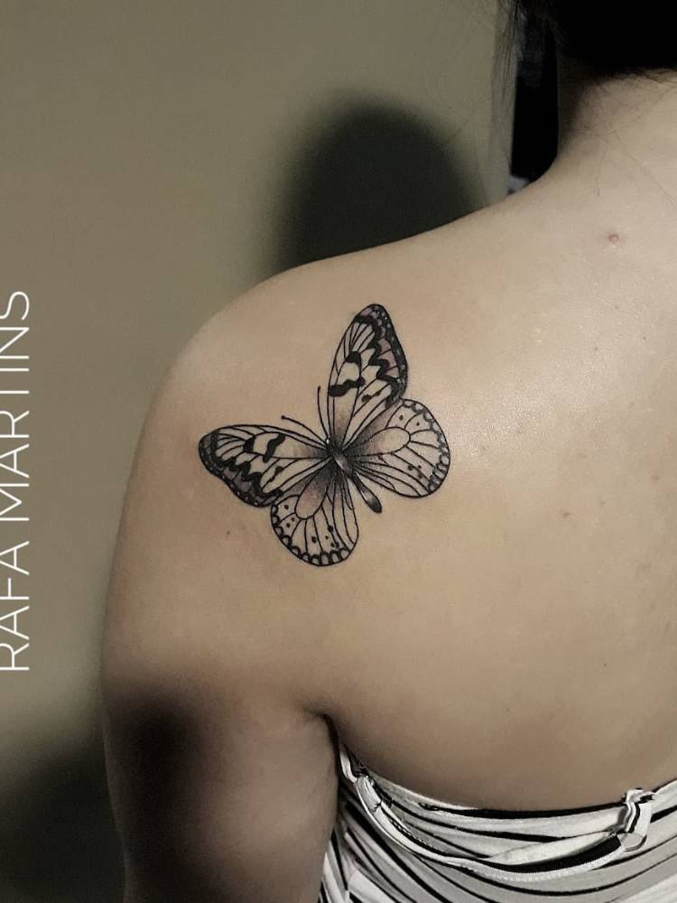 Mulher de pele clara de costas com tatuagem de borboleta na parte inferior do ombro, com traços finos e grossos em preto
