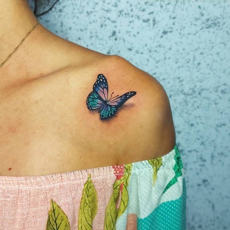 Mulher de pele clara usando blusa de ombro a ombro colorida e tendo tatuagem de borboleta azul sombreada no ombro
