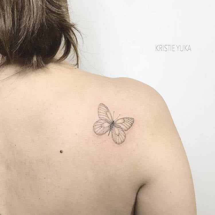 Mulher de pele clara e cabelo curto de costas com tatuagem delicada fine line de borboleta 