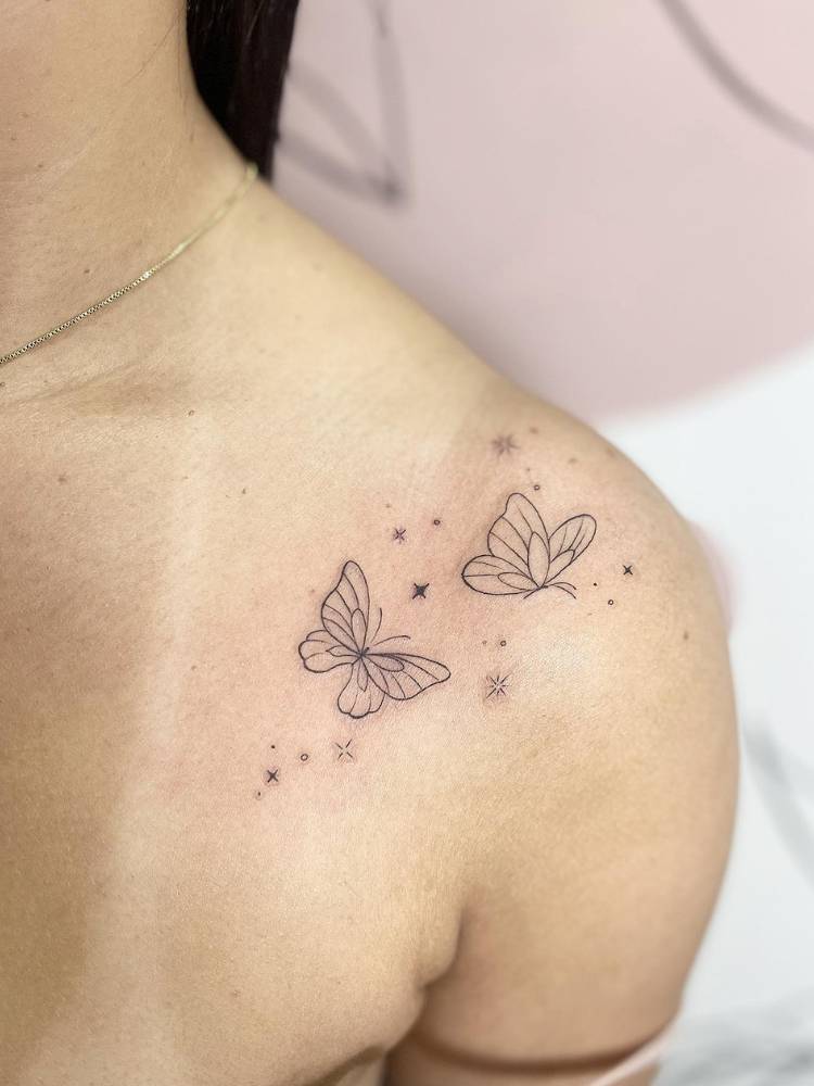 Mulher de pele clara com tatuagem delicada de duas borboletas e estrelas no ombro