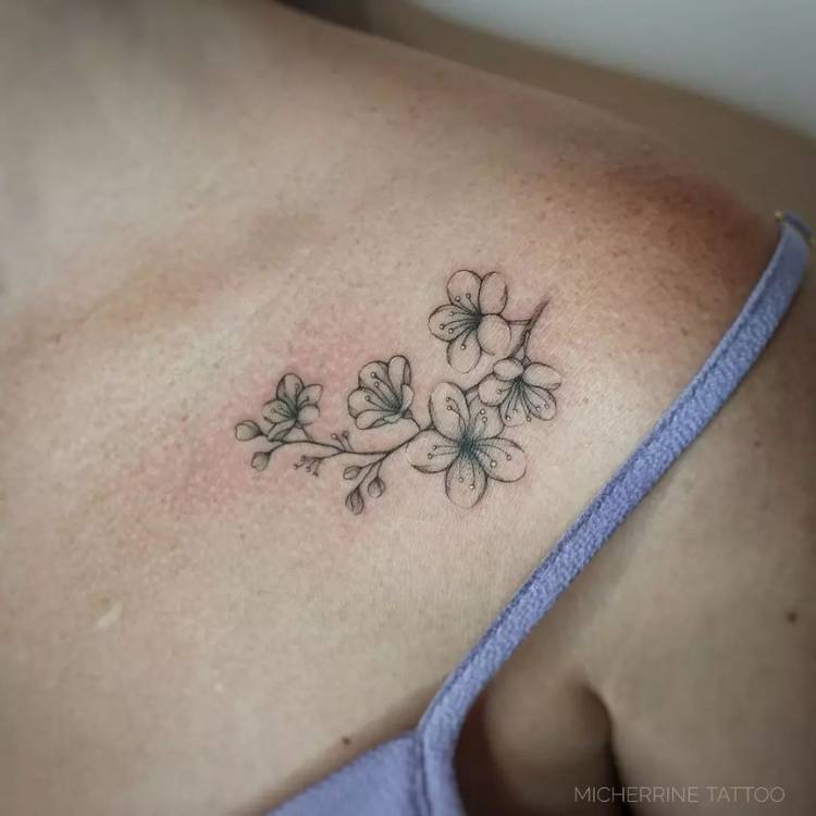 Mulher de pele clara com regata cinza e tatuagem de ramo de flores em fine line com detalhes em amarelo claro