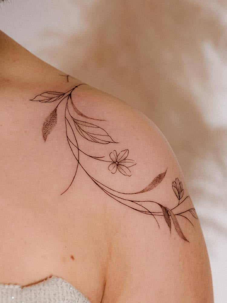 Mulher de pele clara com ombro tatuado com ramos de flores ao redor dessa parte do corpo