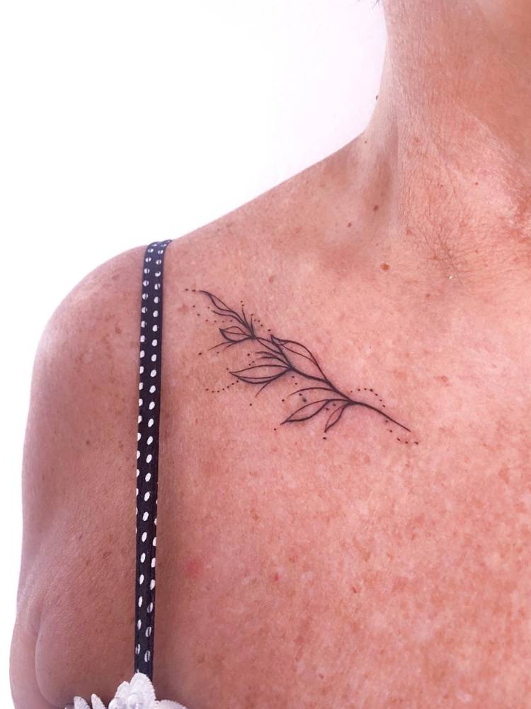 Mulher de pele clara com muitas sardas e tatuagem delicada de ramos no ombro