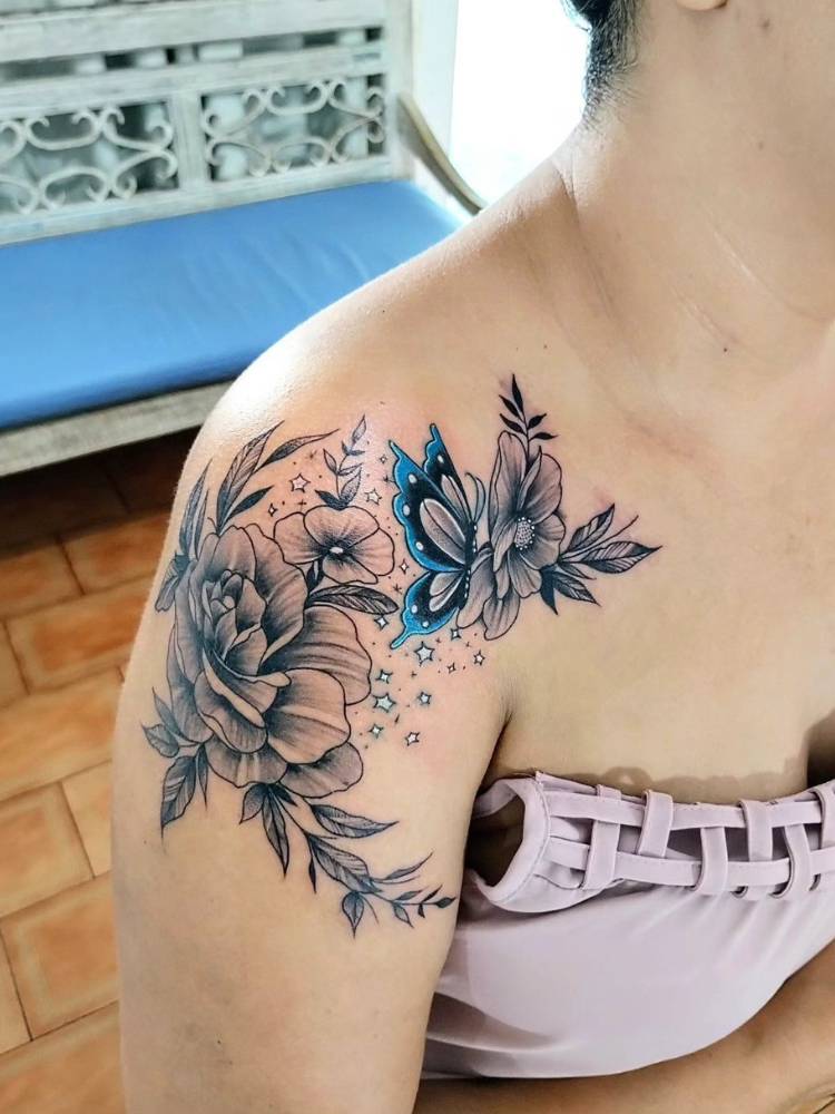 Mulher de pele clara com blusa rosa antigo e tatuagem de flores sombreadas com borboleta azul no ombro