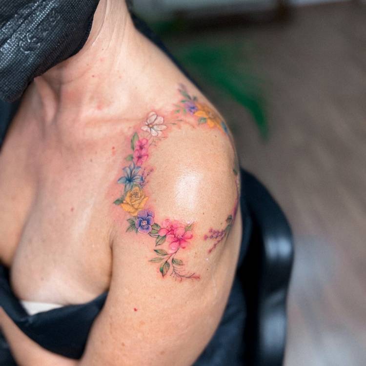 Mulher de pele clara com blusa azul e tatuagem de ramos de flores coloridas ao redor do ombro