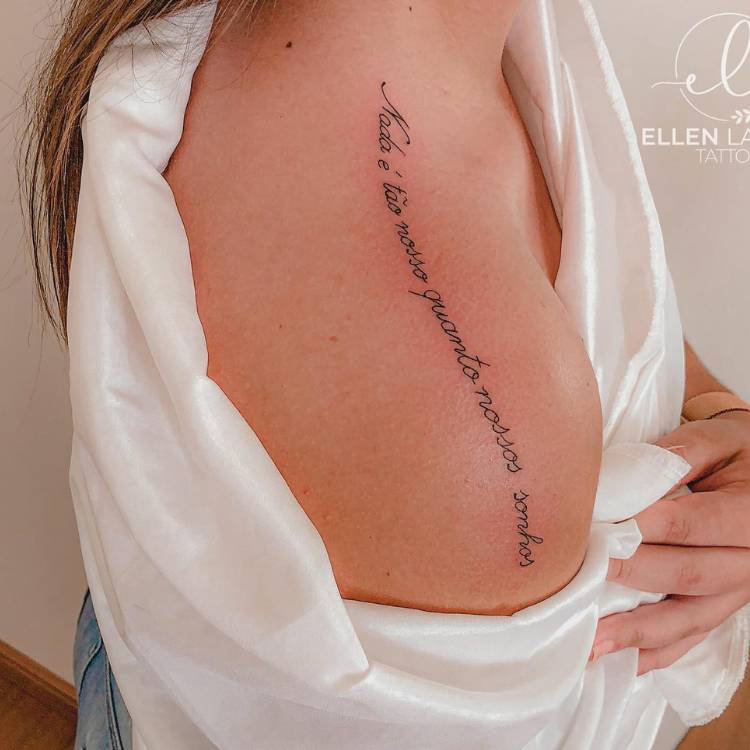 Mulher de pele clara com tatuagem de frase no ombro do pescoço até o começo do braço, com a frase "Nada é tão nosso quanto nossos sonhos"