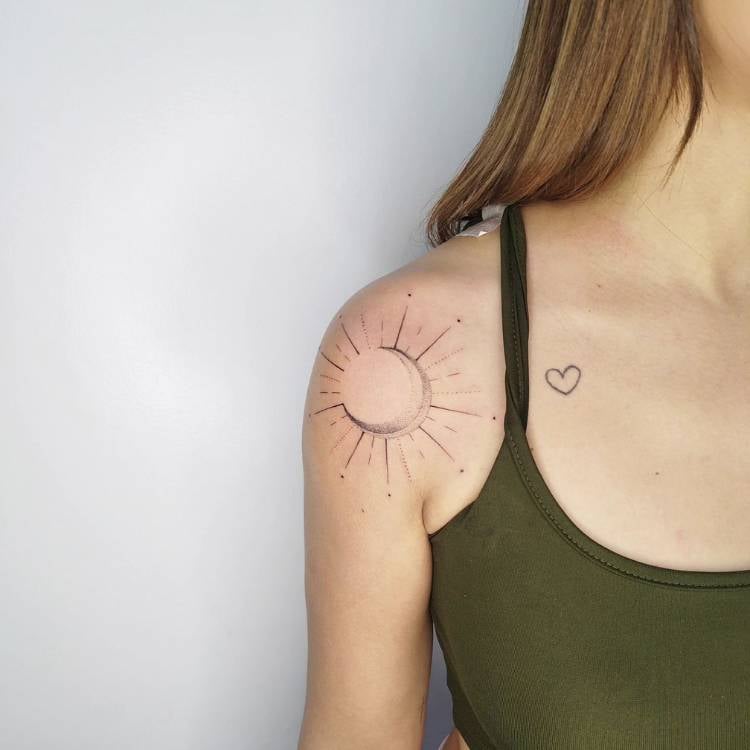 Mulher de pele clara usando regata verde com tatuagem de coração próxima ao colo e tatuagem de sol fine line no ombro