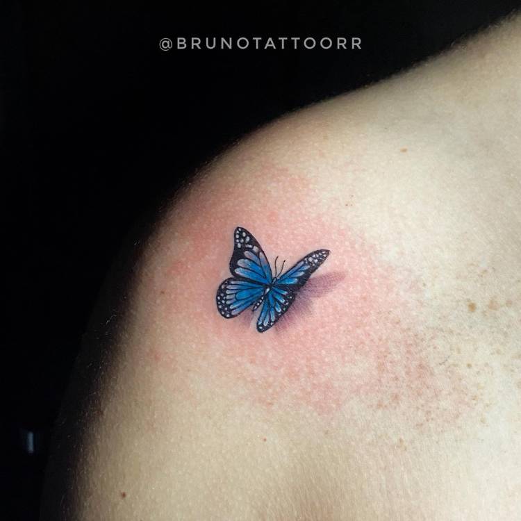 Mulher de pele clara com tatuagem realista de borboleta azul sombreada no ombro