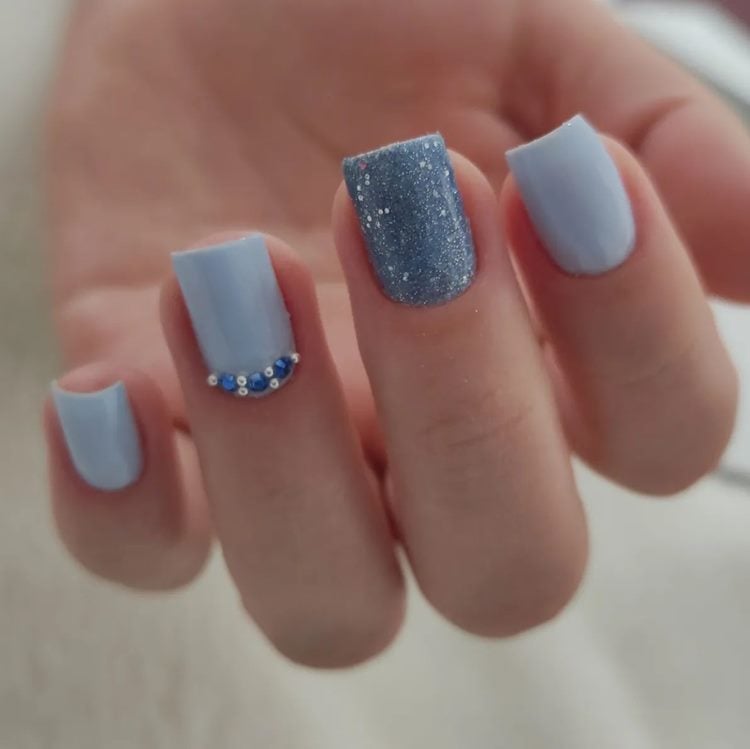 Unha azul pastel, filha única com pedraria na cutícula. dedo do meio com glitter azul 
