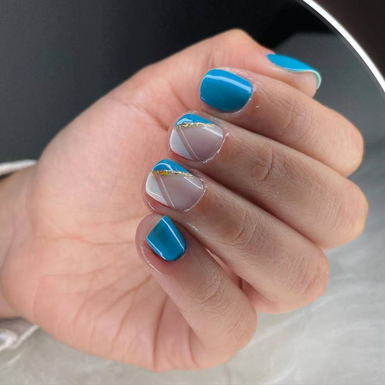 Unhas decoradas em tons de azul com folha de ouro