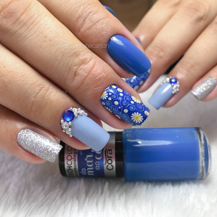 Unhas decoradas em tons de azul com glitter Prateado pedraria e adesivo de flor
