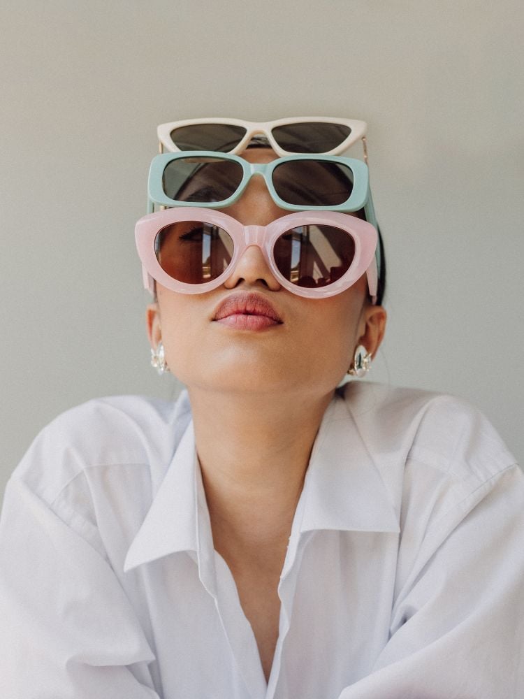 mulher de camisa branca usando 3 óculos de sol de cores diferentes