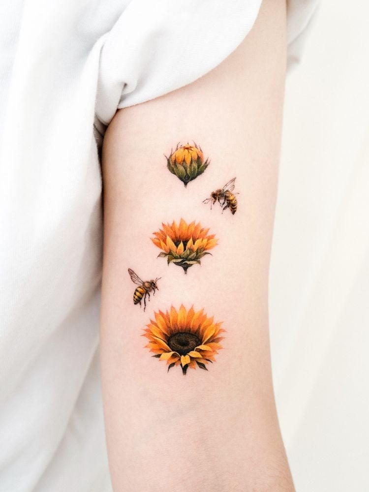 foto de braço com tatauagem de três girassóis amarelos com duas abelhas voando em volta