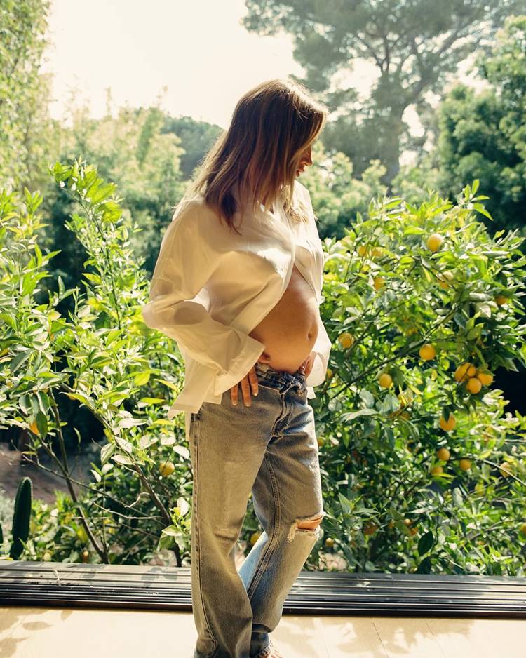 Atris Ashley Tisdale de The Suite Life of Zack & Cody grávida em 2024, usando camisa branca e calça jeans em local com pé de fruta 