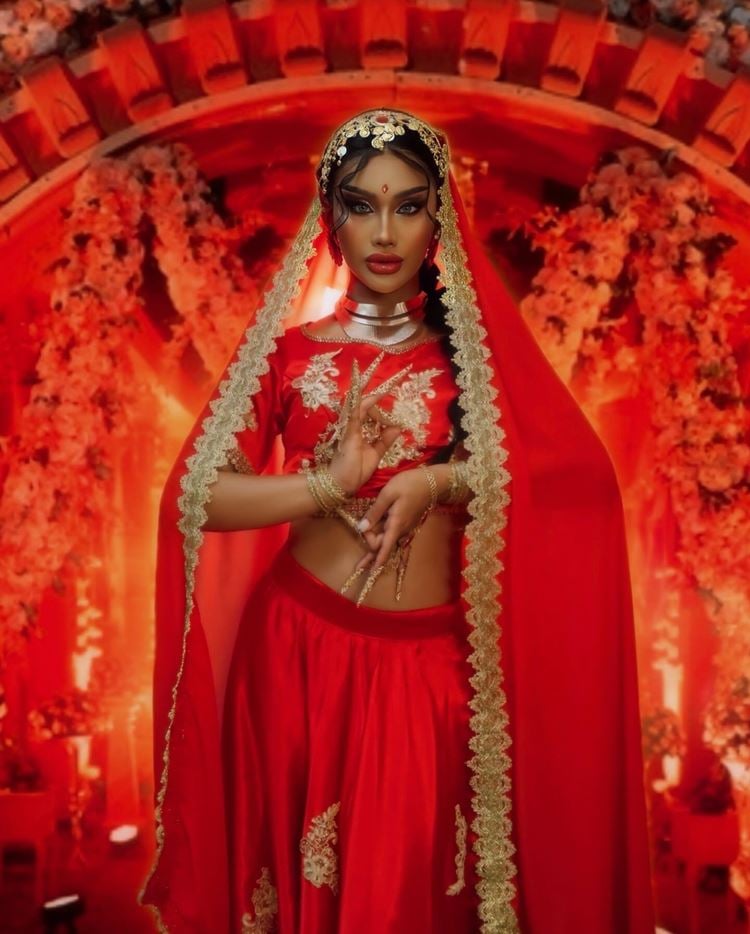 Pessoa com roupa indiana vermelha e dourada e make nude com olhos marcados e com batom vermelho